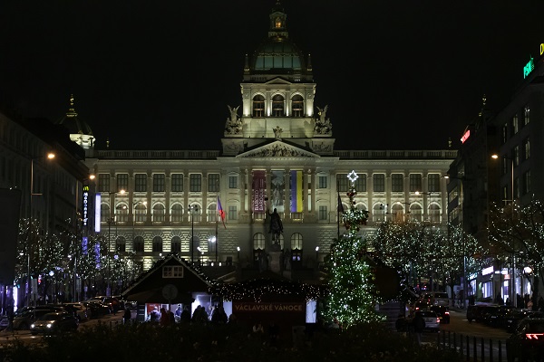 Columned building with flags and statue in front in a square at night lit by Christmas lights